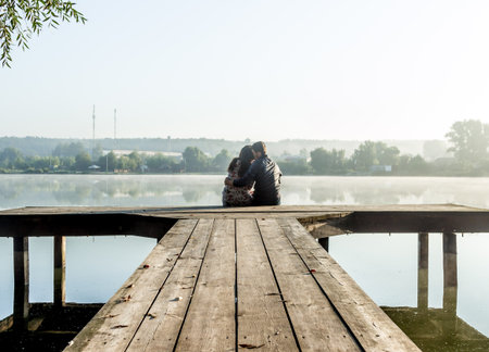 romantic young couple sitting on wooden bridge into the water.の写真素材