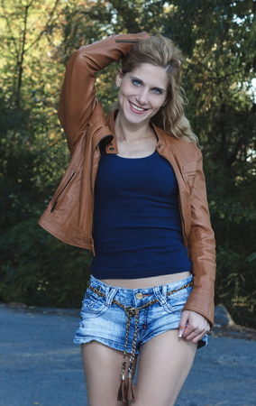 blonde girl in a brown leather jacket and denim shortsの写真素材