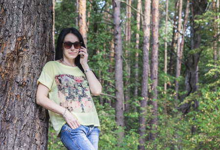 elegant brunette girl in autumn near a tree talking on the phoneの写真素材