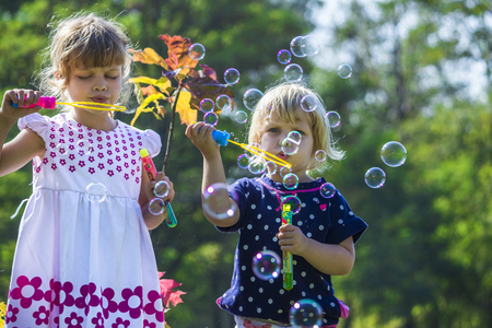 Two funny little sisters blowing soap bubbles outdoors on beautiful summer dayの写真素材