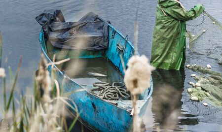 Fishing on the lake. Man pulls a fish net, autumn day, wtih boatの写真素材