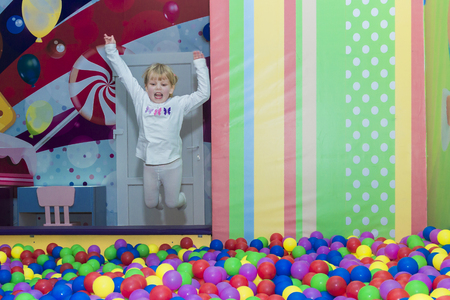 girl jumping into the colorful balls. playing in the park playground.の写真素材