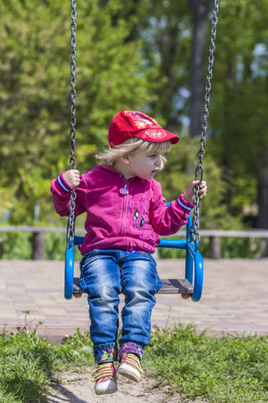 Cute little girl on a swing. Smiling child playing outdoors.の写真素材