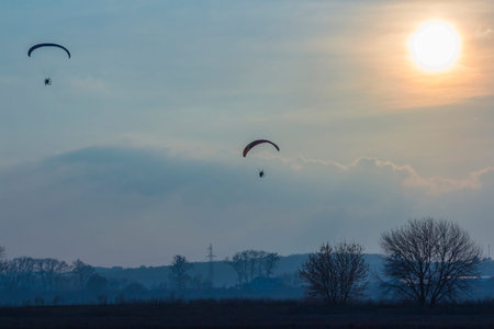paramotor glider flying in the sky over beautiful countryside field landscape at sunset