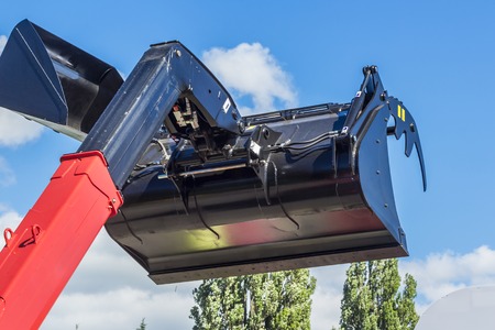 Raised bucket of an excavator over blue skyの写真素材