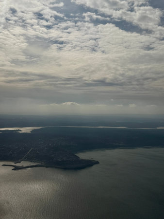Aerial view of coastline and harbor landscape with dramatic clouds and sunlight reflecting on the sea.の写真素材
