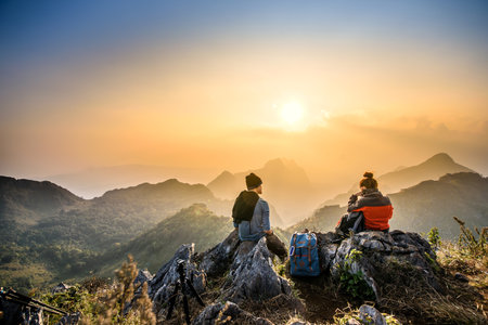 couple hiking at sunset mountain with heavy backpack golden hour for photographyの写真素材