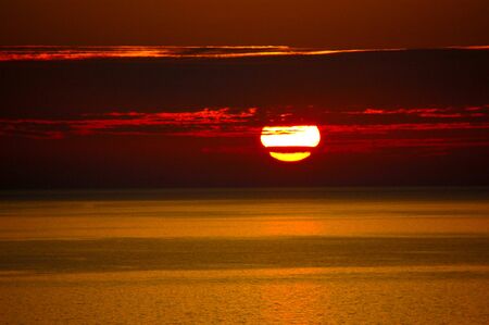 Red Lighthouse with Light Beam at Sunset. The top of a red and metallic lighthouse with light beam at sunset with cloudsRed Sunset on the sea with clouds.の写真素材