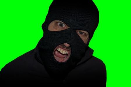 man close up thief in a mask and a blue shirt on a yellow background looks slyly to the camera. Mimicry. Photo shoot. Evil criminal wearing balaclavaの写真素材