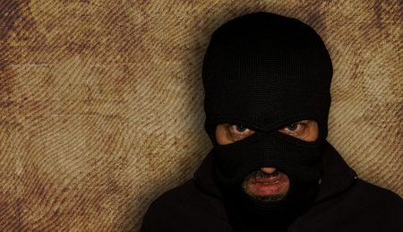 man close up thief in a mask and a blue shirt on a yellow background looks slyly to the camera....