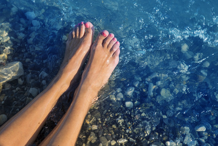 Young and beautiful female bare feet with red painted nails or pedicure standing on a beach, waves bathes her feet. Summer vacation concept.の写真素材