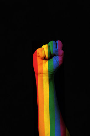 Photo of a raised fist colored with the rainbow gay pride dark background