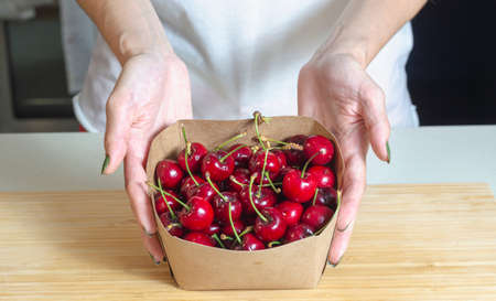 Female hand holding cardboard box full of sweet cherries at home Eco-friendly fruits nature love ecology environment Red Fruitsの写真素材