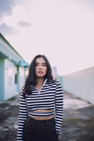 The girl has a skin color of honey or tan. Wearing black and white striped clothes Street photography poses on rooftopの写真素材