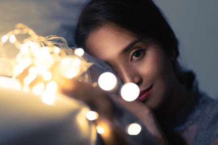 A young woman playing with sparkling lights or fairy light In a room with a dim yellow light. She smiled gently With pleasure.の写真素材