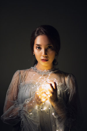A young woman standing and hold sparkling lights or fairy light with a dim yellow light on a dark backgroundの写真素材