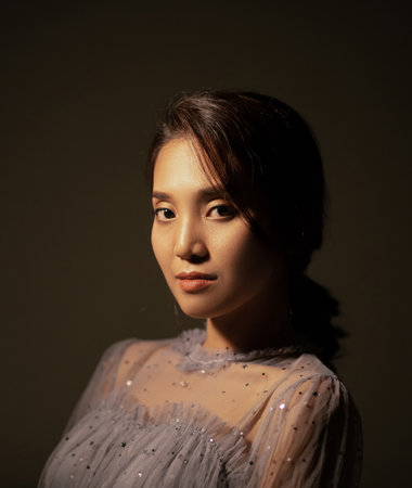 A close up of an asian woman's face In vintage fancy dress In dim light and dark background, She is smiling and looking at you.の写真素材