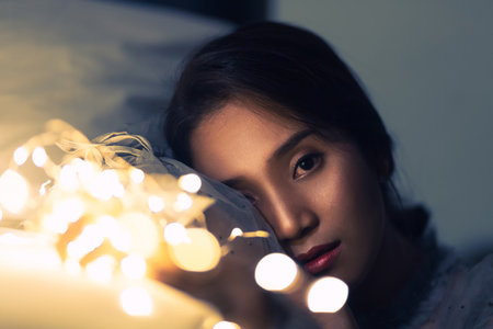 A young woman playing with sparkling lights or fairy light In a room with a dim yellow light. She showed sensitivity and stared at you.の写真素材