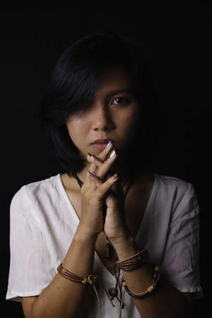 Asian short black haired woman Wearing jewelry made of leather and stone On her face, there is a small freckle On a black background and shadowsの写真素材