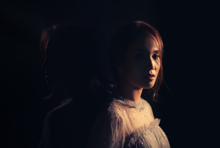 Woman in fancy dress Stand in the dark Her back has a shadow that looks like another woman. Under the concept of different emotions of darkness and brightnessの写真素材