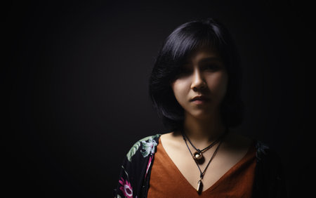 Asian short black haired woman Wearing jewelry made of leather and stone On her face, there is a small freckle On a black background and shadowsの写真素材