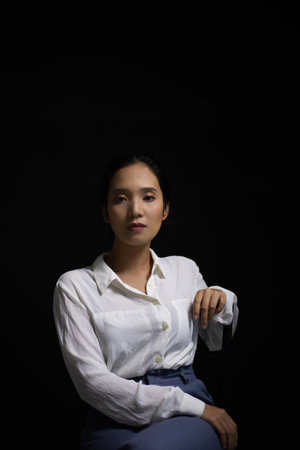 An Asian woman wearing a white long-sleeved shirt with an office style Korean fashion girl Poses shooting on a black backgroundの写真素材