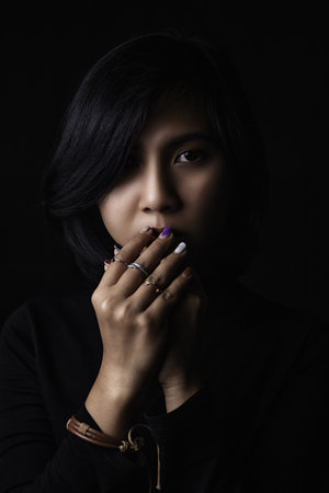 Asian short haired girl Wearing a black long-sleeved shirt And jewelry made of metal and leather, sad faces on a black background and shadowsの写真素材