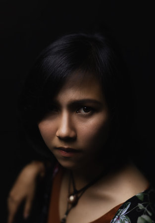 Asian short black haired woman Wearing jewelry made of leather and stone On her face, there is a small freckle On a black background and shadowsの写真素材
