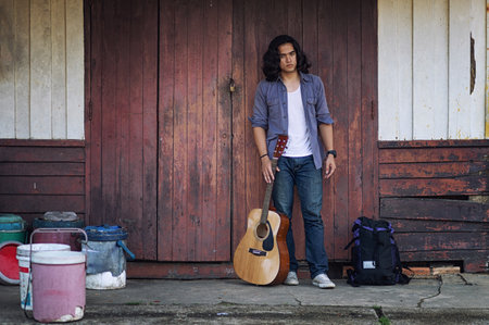 Long haired man that looks cool He is a traveler or nomadic musician who is backpacking and guitars, walking near train track in rural.の写真素材
