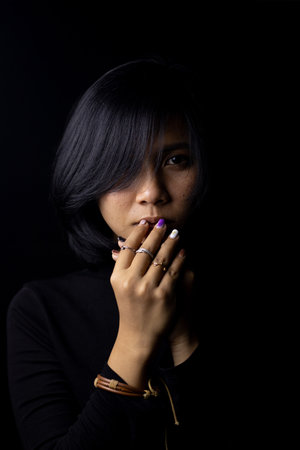 Asian short haired girl Wearing a black long-sleeved shirt And jewelry made of metal and leather, sad faces on a black background and shadowsの写真素材