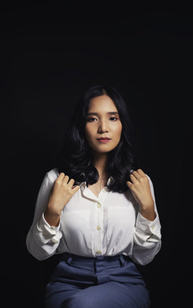 An Asian woman wearing a white long-sleeved shirt with an office style Korean fashion girl Poses shooting on a black backgroundの写真素材