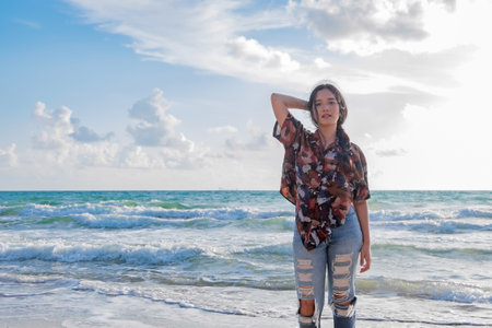 Portrait of a cute asian teenager young woman stand against blue sky and cloud background. wind blows her hair. filtered image to vintageの写真素材