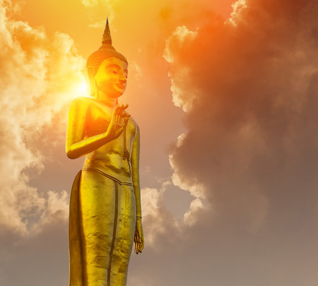 Standing Buddha statue against on Golden sky with sunlight in background.の写真素材