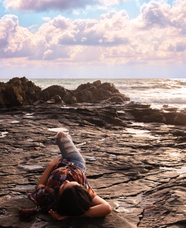 Woman lying down on beautiful texture of rock near the beach at sunrise. Woman sunbathing on tropical paradise beach with beautiful sunrise sky. Summer vacation.の写真素材