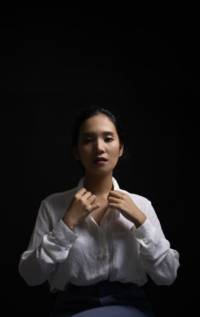An Asian woman wearing a white long-sleeved shirt with an office style Korean fashion girl Poses shooting on a black backgroundの写真素材