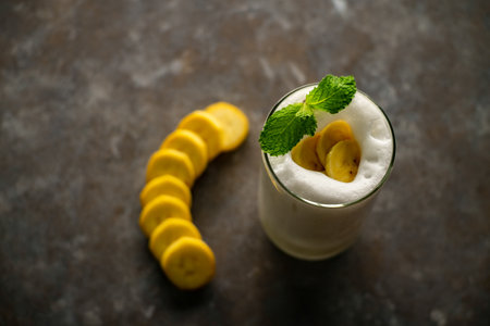 Banana Smoothie on a dark grey table and a piece of banana slide in a glassの写真素材