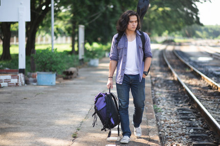 Long haired man that looks cool He is a traveler or nomadic musician who is backpacking and guitars, walking near train track in rural.の写真素材
