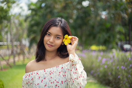 Beautiful asian short hair girl with perfect tan skin smile happily She used the yellow flowers to tuck at her ear,  The beautiful face of a Thai woman.の写真素材