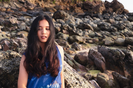 Asian woman, tan skin, she has natural long hair, chocolate color, spreading by the wind, wearing a tie dye shirt. Standing on the rocks at the seaの写真素材