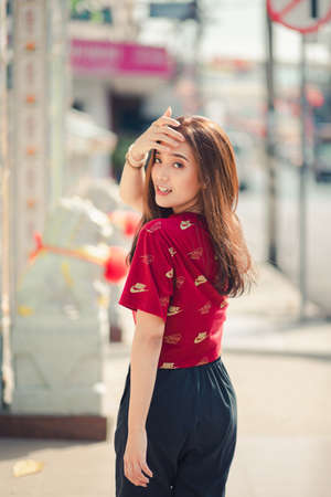 Hatyai, Thailand - Feb 3, 2020: Brown long haired girl Wearing a red T-shirt and Nike warm pants on a casual day, she is walking in a sunny city.のeditorial素材