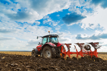 Farmer plowing stubble field with red tractor
