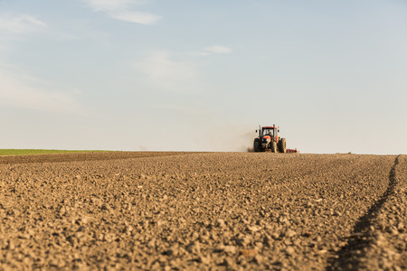 Farmer in tractor preparing land with seedbed cultivator as part of pre seeding activities in early spring season of agricultural works at farmlands.の写真素材