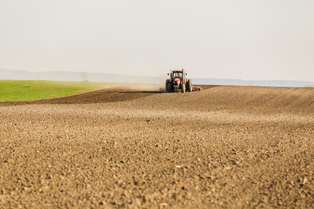 Farmer in tractor preparing land with seedbed cultivator as part of pre seeding activities in early spring season of agricultural works at farmlands.の写真素材