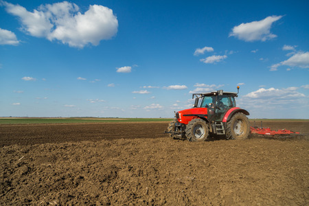 Farmer in tractor preparing land with seedbed cultivator as part of pre seeding activities in early spring season of agricultural works at farmlands.の写真素材