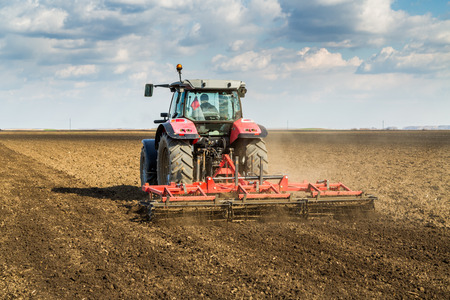 Farmer in tractor preparing land with seedbed cultivator as part of pre seeding activities in early spring season of agricultural works at farmlands.の写真素材