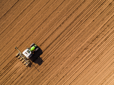 Aerial shot of a farmer seeding, sowing crops at field. Sowing is the process of planting seeds in the ground as part of the early spring time agricultural activities.の写真素材