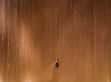 Aerial shot of a farmer seeding, sowing crops at field. Sowing is the process of planting seeds in the ground as part of the early spring time agricultural activities.の写真素材