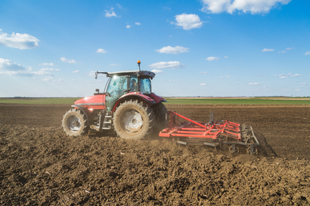 Farmer in tractor preparing land with seedbed cultivator as part of pre seeding activities in early spring season of agricultural works at farmlands.の写真素材