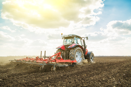 Farmer in tractor preparing land with seedbed cultivator as part of pre seeding activities in early spring season of agricultural works at farmlands.の写真素材
