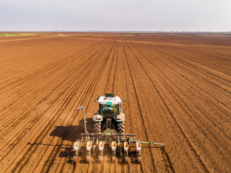 Aerial shot of a farmer seeding, sowing crops at field. Sowing is the process of planting seeds in the ground as part of the early spring time agricultural activities.の写真素材